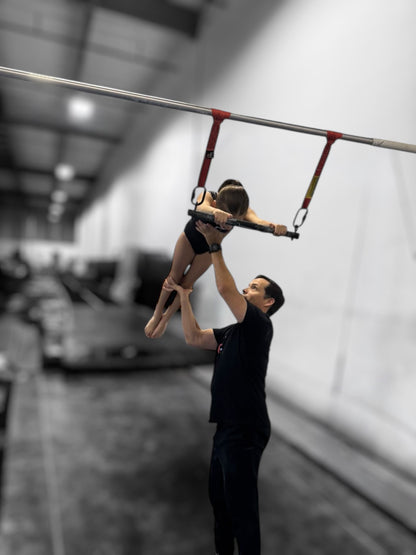 Person assisting another person on a high bar in an indoor setting